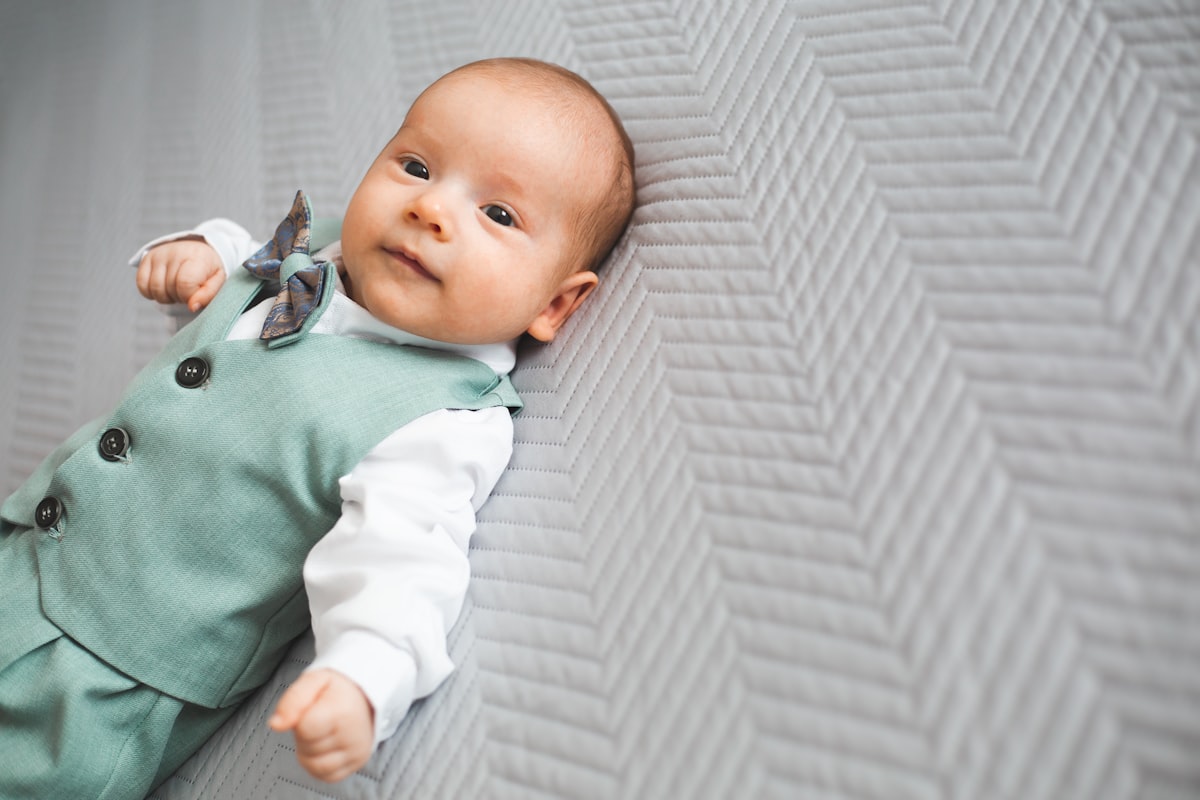 Young baby boy dressed up, lying on his back on bed, looking towards camera. related to Creating a Dream Nursery: The Ultimate Guide to Boy Crib Bedding