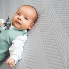 Young baby boy dressed up, lying on his back on bed, looking towards camera. related to Creating a Dream Nursery: The Ultimate Guide to Boy Crib Bedding