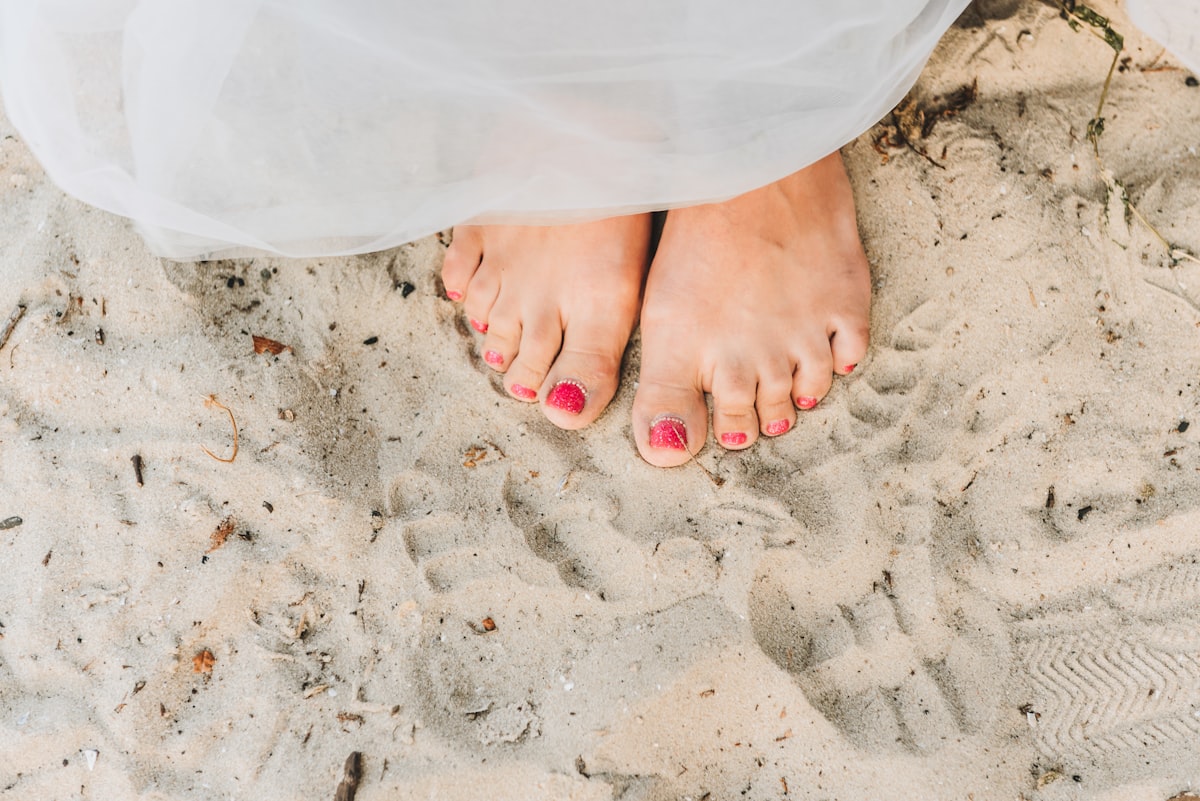 Young caucasian woman's feet with nice manicure on sandy beach, close up related to Nail Bed Infection: Understanding the Causes, Symptoms, and Treatment Options