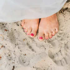 Young caucasian woman's feet with nice manicure on sandy beach, close up related to Nail Bed Infection: Understanding the Causes, Symptoms, and Treatment Options