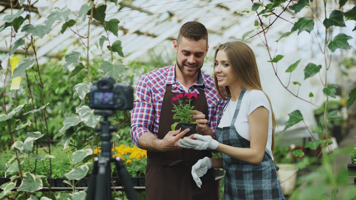 Young smiling blogger couple florist in apron holding flower talking and recording video blog for online vlog about the gardening related to Transform Your Yard with DIY Garden Beds