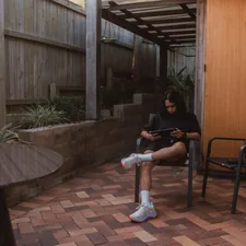 Young woman on patio using tablet in a fenced yard. related to Protect Your Outdoor Living Space with Chiminea Decking Protectors